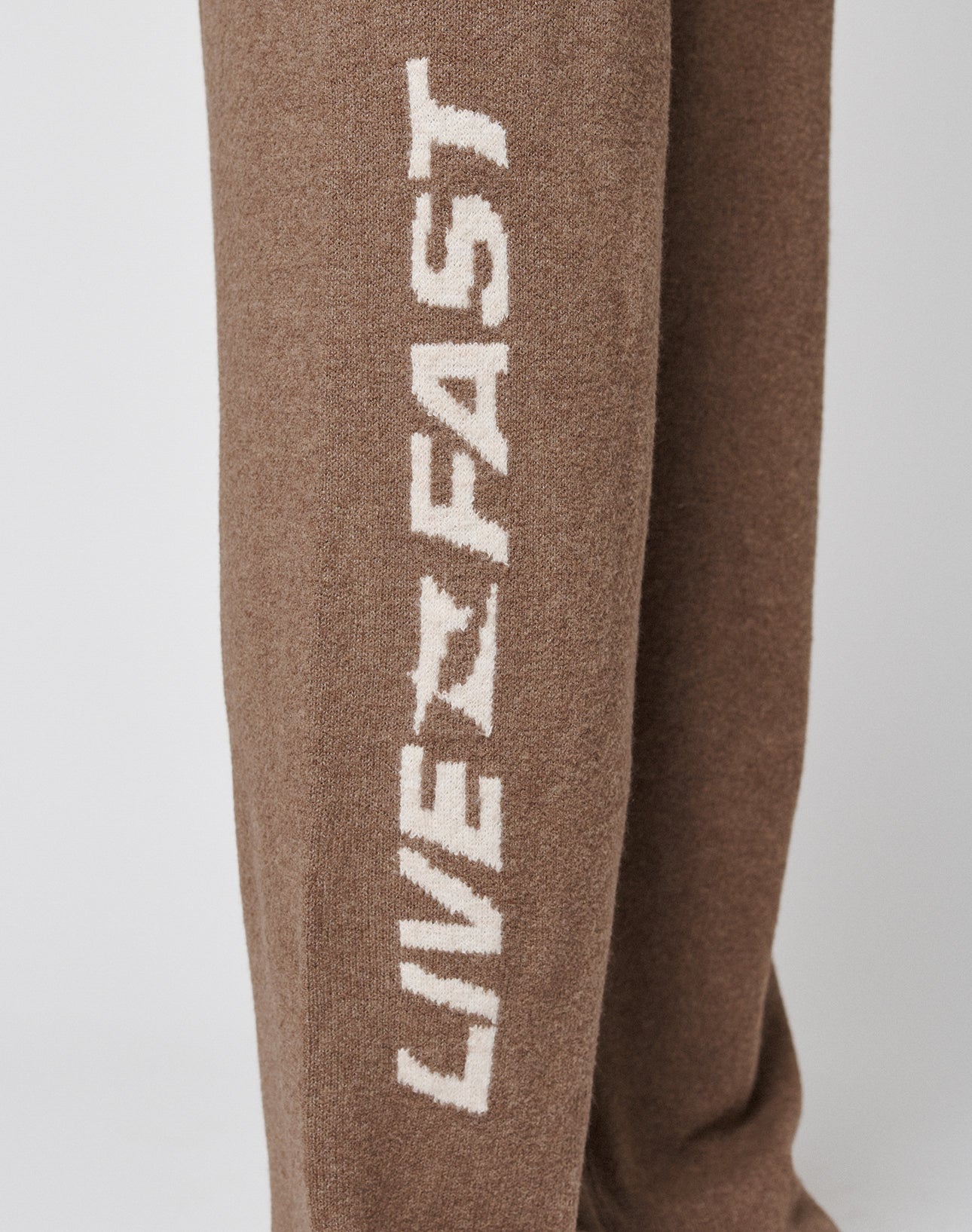 A close-up of the Live Fast Boucle Pants by LIVE FAST DIE YOUNG, featuring a wide fit and vertical white "LIVE FAST" text along the side of the brown leg.