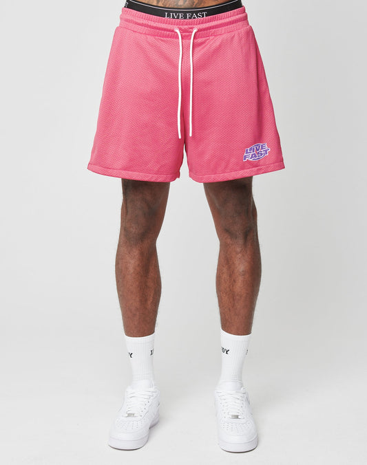 A person wearing LFDY Oval Mesh Shorts by LIVE FAST DIE YOUNG in pink, featuring an elastic waistband and LIVE FAST text, stands against a plain light background. Only the lower half with white socks and sneakers is visible.