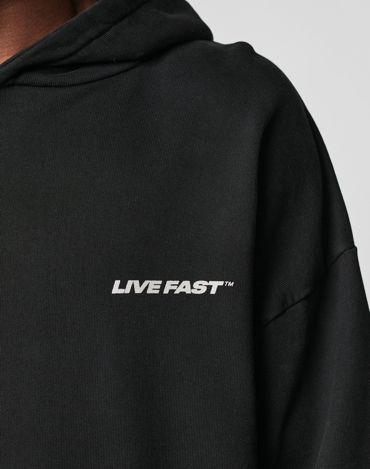 Close-up of the LFDY Hardwear Hooded by LIVE FAST DIE YOUNG, an oversized black hoodie made from premium cotton with LIVE FAST™ in white on the chest. Only part of the hoodie and the wearer’s neck are visible.