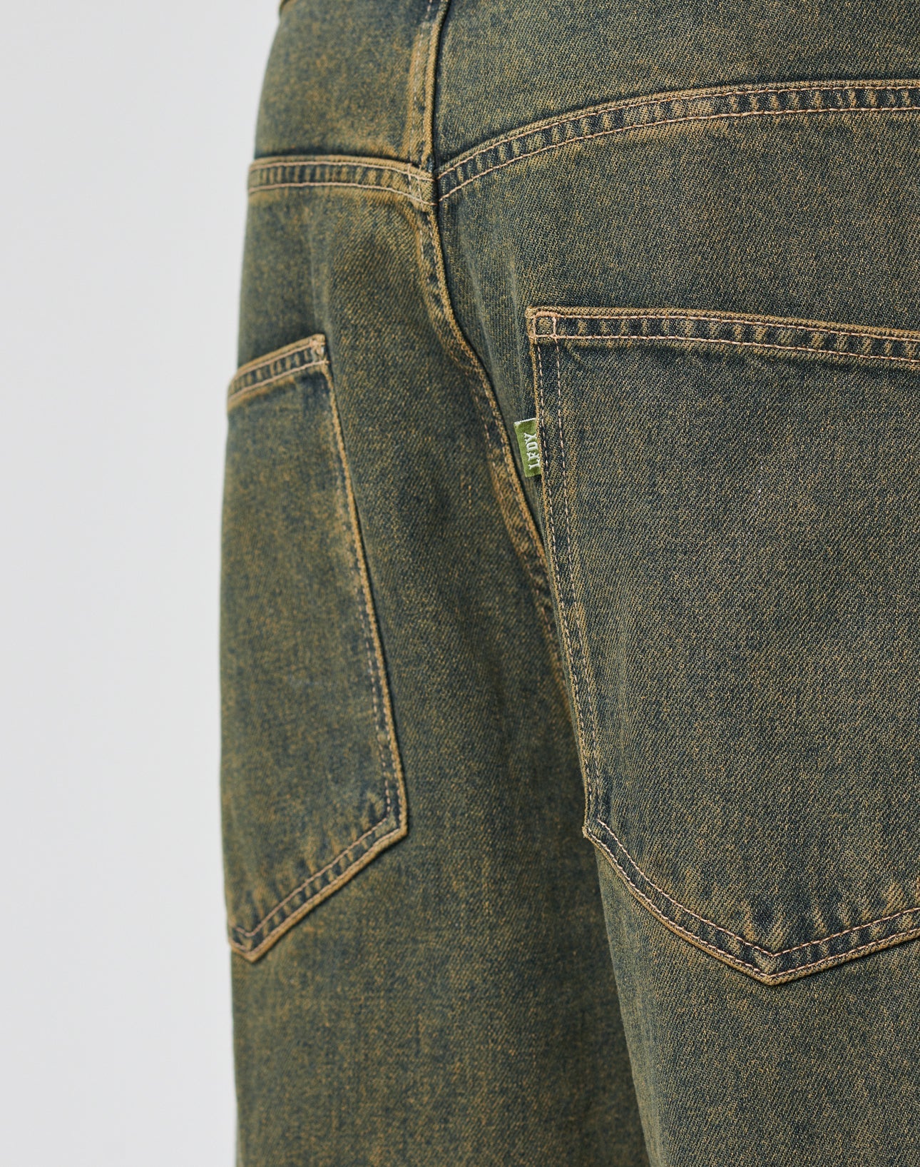 Close-up of the LFDY Baggy Denim by LIVE FAST DIE YOUNG in blue-green, featuring two large back pockets with yellow stitching, a small green tag, 100% Baumwolle material, a baggy fit, and a wide straight leg.