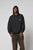 A person wears a black LFDY Hardwear Hooded by LIVE FAST DIE YOUNG with the hood up and chest logo, paired with loose-fitting faded brown Oversize Fit pants, standing against a plain light gray background. The hoodie is 100% Baumwolle.