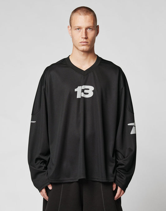A person with short hair wears the LIVE FAST DIE YOUNG Live Fast Jersey, a loose-fitting, long-sleeve black oversize shirt with the number 13 in white on the chest and sleeve numbers, standing against a plain light background.