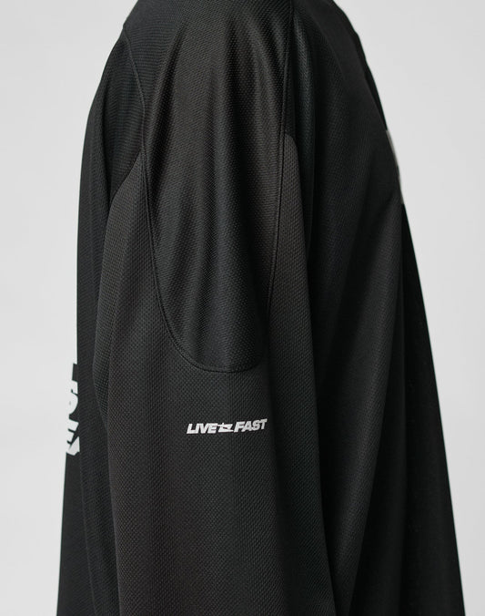 Close-up of the Live Fast Jersey by LIVE FAST DIE YOUNG—an oversized black long-sleeve shirt with LIVE FAST in a white reflective print on the upper sleeve. Made of breathable polyester athletic fabric. Plain, light background.