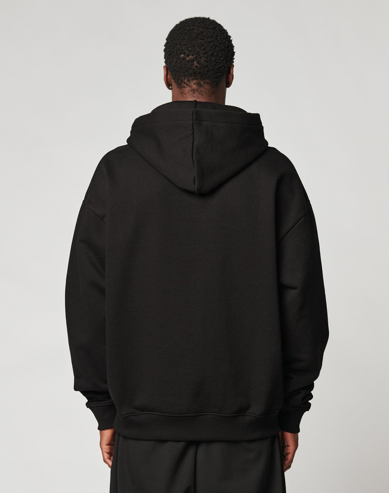 A person faces away from the camera, wearing the LIVE FAST DIE YOUNG Live Fast Plain Hooded black oversize hoodie and matching soft Baumwolle pants, set against a plain light background.