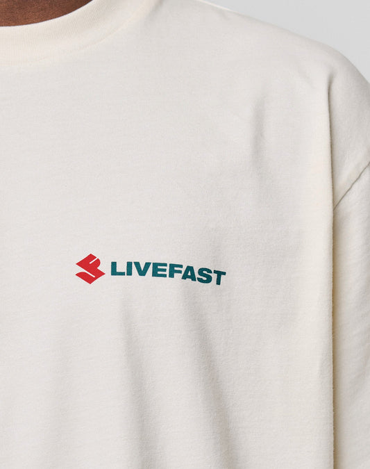 Close-up of the LFDY Dealership Tee by LIVE FAST DIE YOUNG, an oversized cream T-shirt made from 100% cotton, with a red geometric logo and bold green "LIVEFAST" print on the left chest.