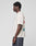 A person with short curly hair stands in profile against a plain background, wearing the LIVE FAST DIE YOUNG LFDY Dealership Tee—an oversize fit off-white T-shirt made from 100% Baumwolle with graphic front and back prints—and dark jeans.