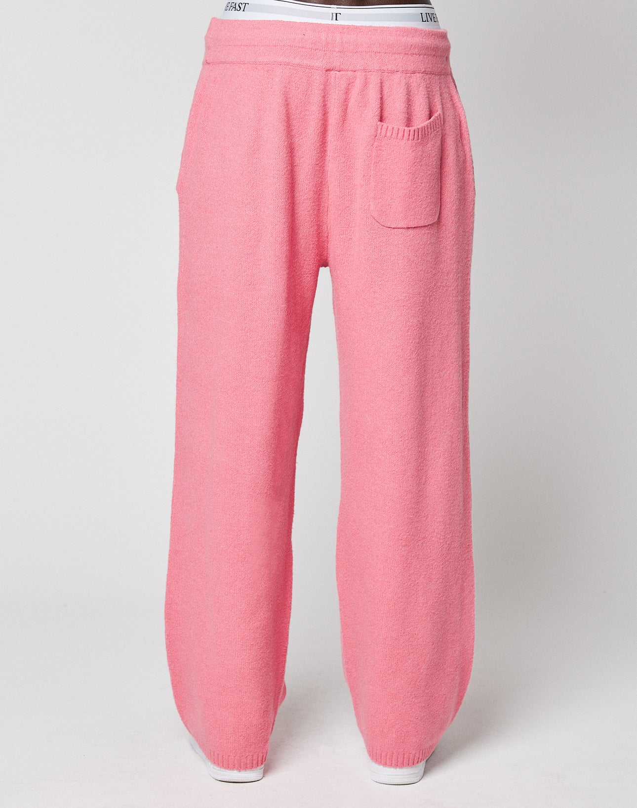 The Live Fast Boucle Pants by LIVE FAST DIE YOUNG are wide fit, pink fleece pants featuring an Elastikbund, side pockets, a straight leg cut, and a small front right patch pocket, shown on a mannequin against a plain background.