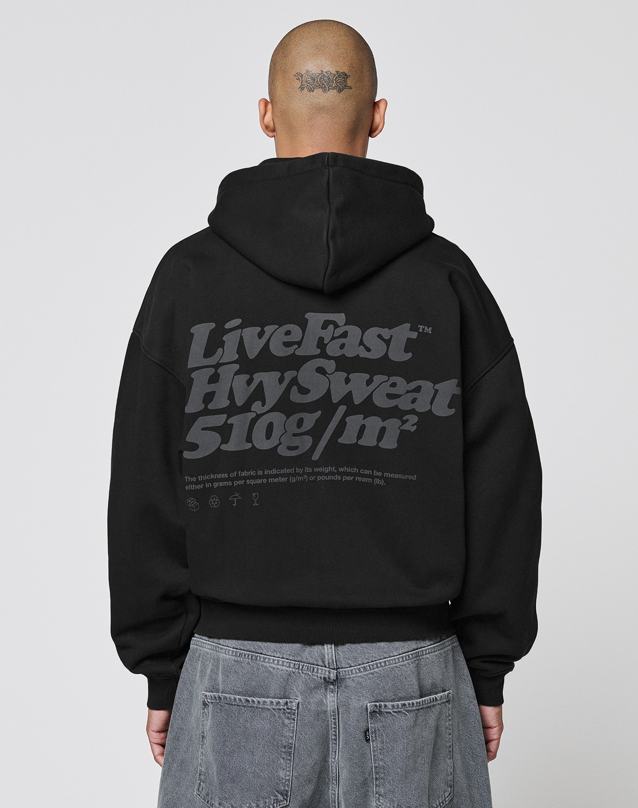 A person with a tattoo on the back of their head wears a LIVE FAST DIE YOUNG Basic 510 Hooded Zip in Oversize Fit with large gray front and back print, paired with gray jeans, facing away from the camera. | model