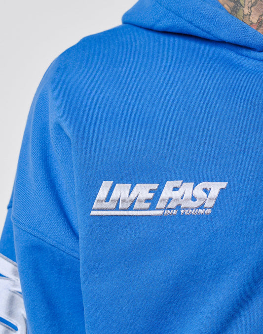 Close-up of the blue LFDY Team Hooded Zip by LIVE FAST DIE YOUNG, featuring white Flaggen-Stick embroidery on the chest with LIVE FAST DIE YOUNG® text. A tattooed neck is partially visible above the oversized hoodie.