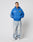 A person stands against a white background wearing the bright blue LFDY Team Hooded Zip by LIVE FAST DIE YOUNG, light blue oversized baggy jeans, and white sneakers. Their hands are in their pockets, with short hair and visible neck tattoos.
