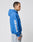 A man with short hair and tattoos models the LIVE FAST DIE YOUNG LFDY Team Hooded Zip in bright blue, featuring EUROPE RUN and Flaggen-Stick sleeve details. He stands in profile against a white background, wearing light-wash jeans and showcasing its oversize fit.
