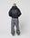 A person with a shaved head, facing away, wears an oversize fit black LIVE FAST DIE YOUNG Basic 510 Hooded Zip hoodie and loose gray vintage-wash jeans, standing against a plain white background.