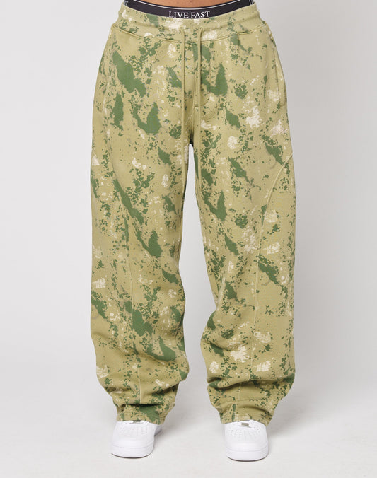 Loose-fitting Camo Wide Jogger pants by LIVE FAST DIE YOUNG in green and beige with a paint-splatter effect and elastic waistband, styled with white sneakers. The visible black waistband features LIVE FAST text.