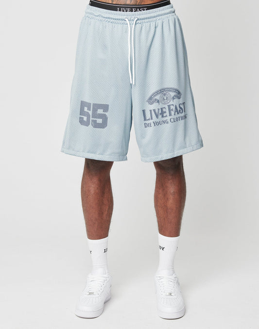 Someone wears the LFDY Loyal Shorts by LIVE FAST DIE YOUNG, featuring a light blue color, elastic waistband, “55” on one leg, and brand graphic/logo on the other, styled with white socks and white sneakers for a cool oversized look.