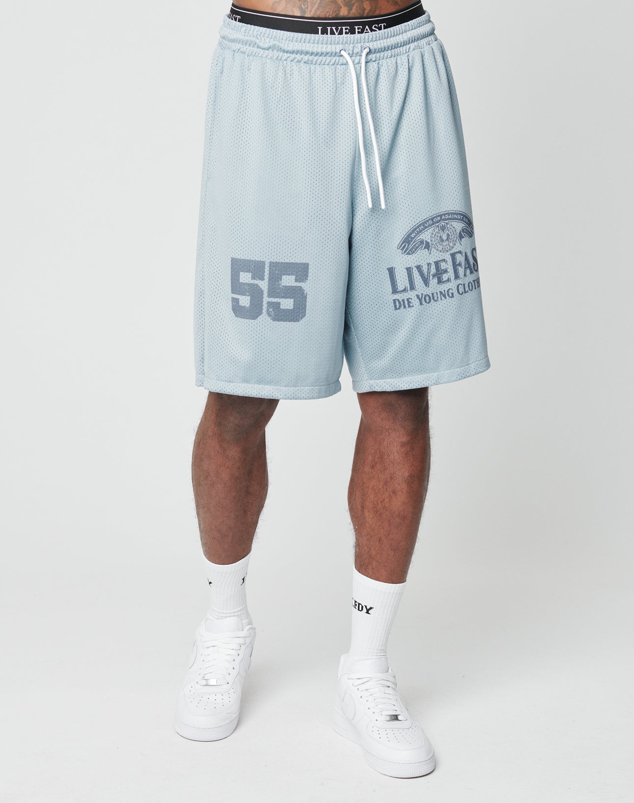 Someone wears LIVE FAST DIE YOUNGs LFDY Loyal Shorts in light blue mesh with an elastic waistband and 55 plus branding on the left leg, featuring an oversized fit, styled with white socks and sneakers against a plain background.