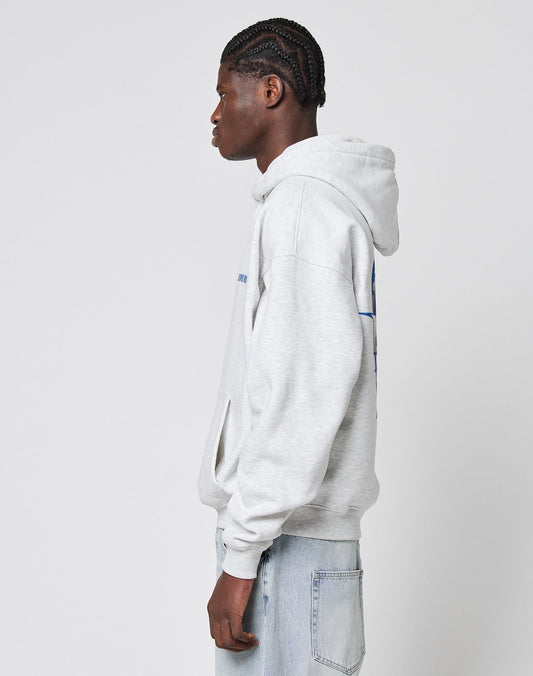 A young man with braided hair stands in profile, wearing an oversize fit light gray LFDY Globe Hooded sweatshirt by LIVE FAST DIE YOUNG, made from a Baumwollemix with Polyester, paired with light blue jeans against a white background.