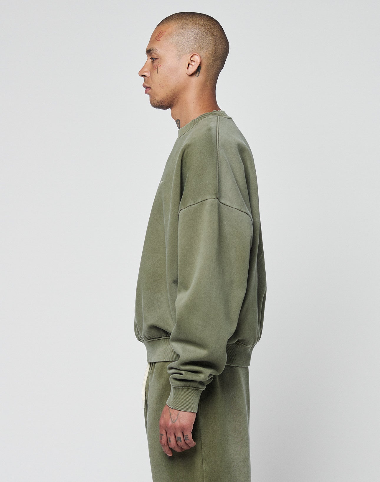 A man with a shaved head stands in profile against a plain light background, wearing the LIVE FAST DIE YOUNG Basic Chest Sweater and oversized matching pants for a relaxed look.