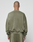 A person with a shaved head, shown from behind against a plain background, wears the LIVE FAST DIE YOUNG Basic Chest Sweater in olive green with matching oversized pants and a subtle faded look.