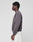 A person in profile faces left, wearing the LIVE FAST DIE YOUNG LFDY Network Sweater—an oversized dark grey cotton sweatshirt with purple front and back prints—paired with light pants, set against a plain light grey background.