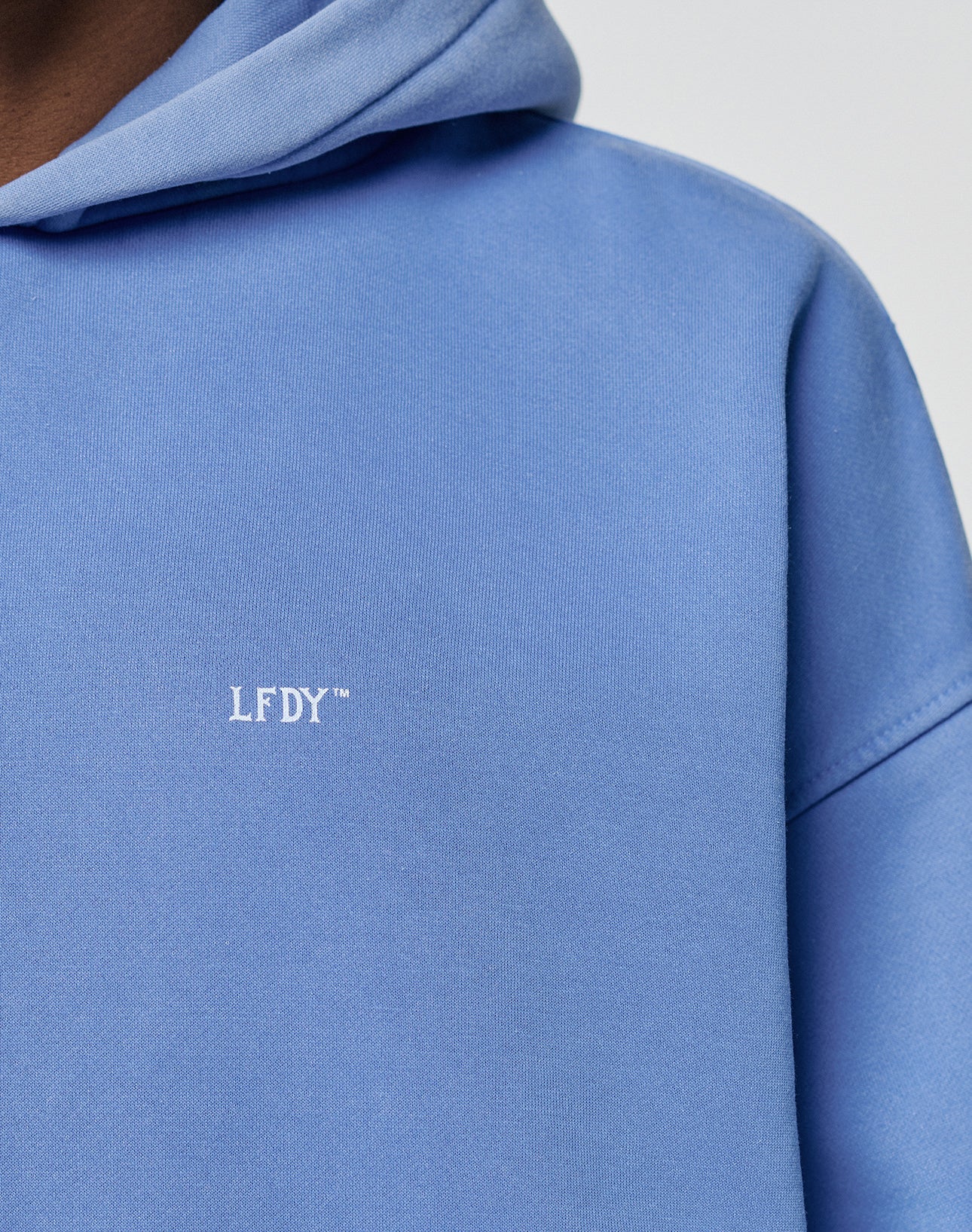 Close-up of the Basic Evidence Hooded by LIVE FAST DIE YOUNG in light blue, with white LFDY print and a stylish fade effect. Only part of the wearers shoulder, chest, and hood is shown.