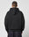 A person with short hair stands with their back to the camera, wearing the LIVE FAST DIE YOUNG LFDY Team Hooded Zip in black with Multilogo Stickereien and dark jeans, set against a plain light grey background.