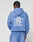 Someone wearing an oversize fit blue Basic Evidence Hooded by LIVE FAST DIE YOUNG with matching shorts stands facing away. The hoodie’s back shows a faded Live Fast print repeated in white, partly covered by a white rectangle graphic.