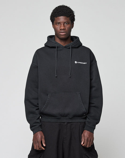 A person stands facing forward wearing a black LFDY Dealership Hooded from LIVE FAST DIE YOUNG with white "LIVEFAST" text on the left chest, matching black pants, and a plain light gray background.