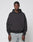 A man with braided hair wears a loose-fitting black LFDY Monaco Boys Hooded by LIVE FAST DIE YOUNG and light blue jeans, standing against a plain light gray background. The hoodie is crafted from Baumwolle Polyester for comfort.