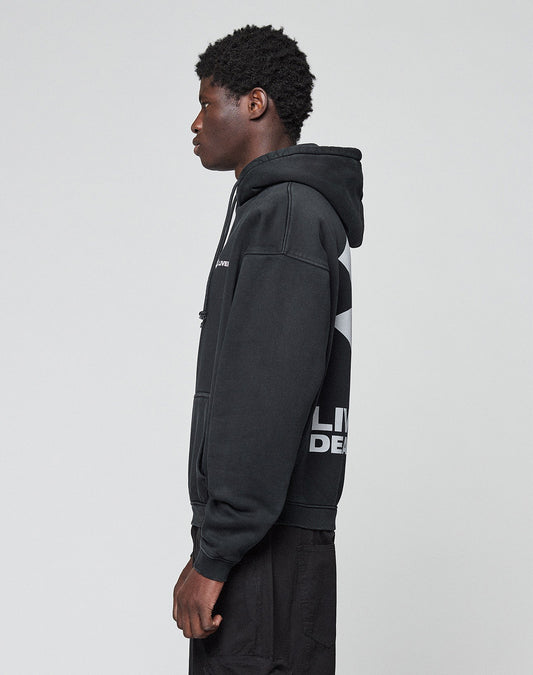 A young person in profile wears the LFDY Dealership Hooded by LIVE FAST DIE YOUNG, an oversize fit black hoodie made of cotton with bold white front and back prints, paired with black pants against a plain light gray background.