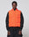 A man wears the LIVE FAST DIE YOUNG Live Fast Cropped Vest in orange with Druckknöpfe over a black sweatshirt and dark pants, standing against a plain light gray background and looking directly at the camera.