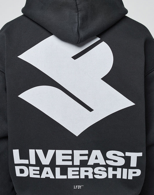 A person wears the oversize fit LFDY Dealership Hooded by LIVE FAST DIE YOUNG in black Baumwolle, featuring a large white abstract logo and bold LIVEFAST DEALERSHIP backprint.