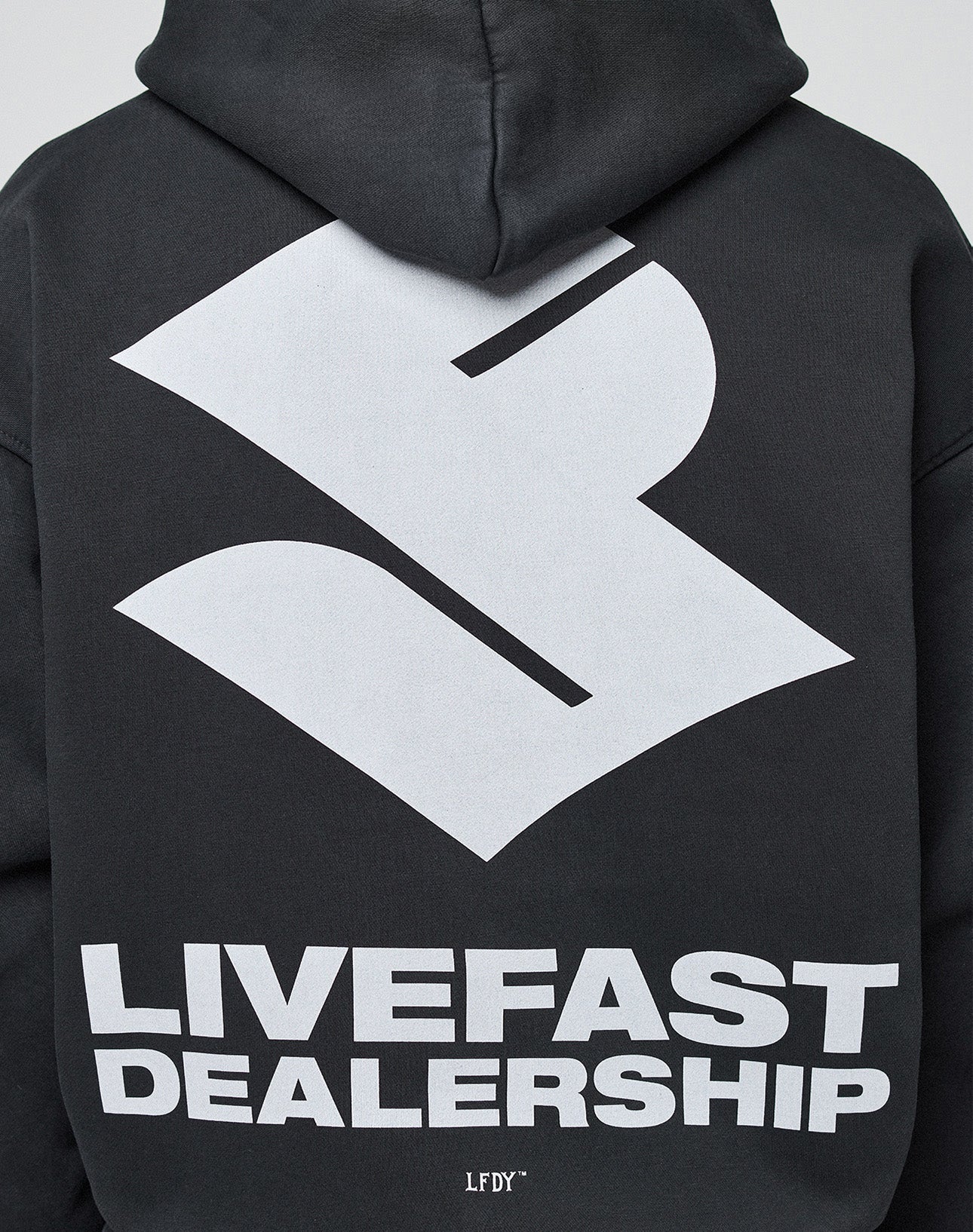 A person wears the oversize fit LFDY Dealership Hooded by LIVE FAST DIE YOUNG in black Baumwolle, featuring a large white abstract logo and bold LIVEFAST DEALERSHIP backprint.