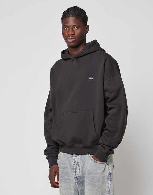 A man in the LIVE FAST DIE YOUNG LFDY Monaco Boys Hooded, featuring an oversize fit and front and back print, pairs it with light blue jeans as he stands against a plain light background, looking at the camera with a neutral expression.