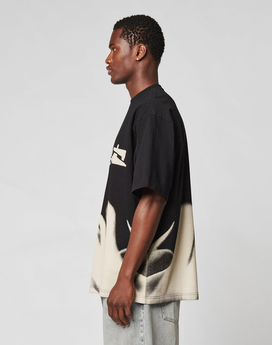 A young man stands in profile against a plain background, wearing the LFDY Mystic Tee by LIVE FAST DIE YOUNG—an oversize fit 100% Baumwolle shirt with bold abstract patterns and striking front and back prints—paired with light gray jeans.