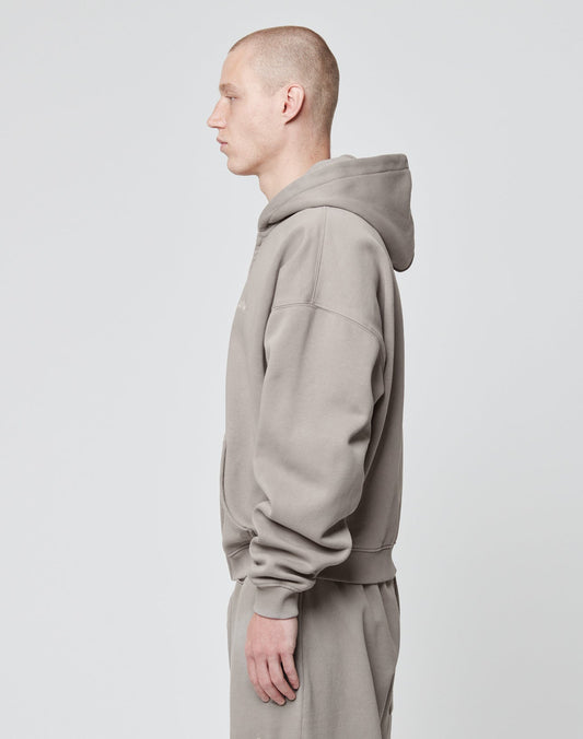 A person with short hair stands in profile, facing left, wearing the LIVE FAST DIE YOUNG Basic Script Hooded Zip and matching sweatpants in light gray against a plain light gray background.