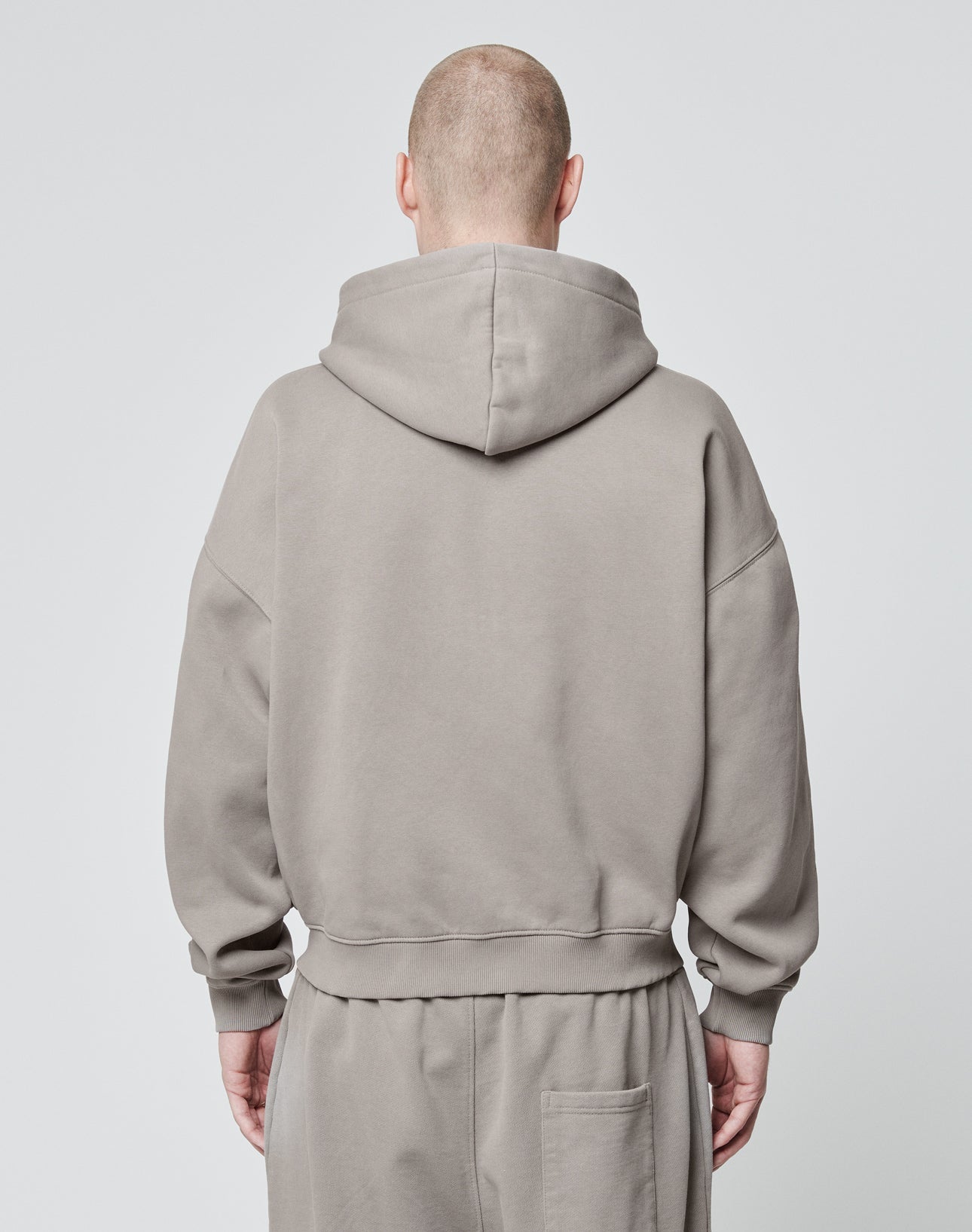 A person with a shaved head is seen from behind wearing the LIVE FAST DIE YOUNG Basic Script Hooded Zip in light gray Vintage-Waschung Baumwolle-Polyester, paired with matching sweatpants, against a plain light background.