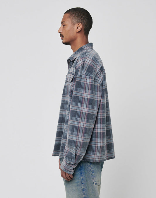A man with short hair wears the LIVE FAST DIE YOUNG Loose Flannel Shirt in blue and gray plaid, made from 100% Baumwolle, styled with light blue jeans and standing in profile against a plain, light background.