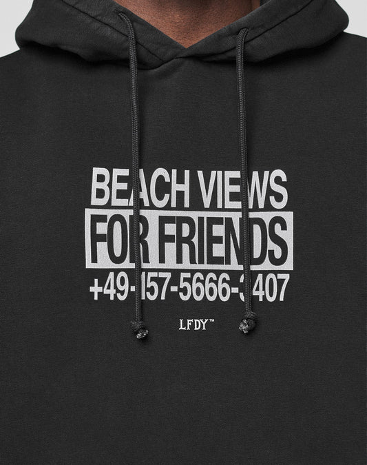 Close-up of the black Live Fast Call Us Hooded by LIVE FAST DIE YOUNG in Oversize Fit, featuring a white BEACH VIEWS FOR FRIENDS +49-157-5666-1407 LFDY™ front print and black drawstrings.