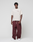 A person stands against a plain background wearing the LIVE FAST DIE YOUNG Basic 210 Tee in oversize beige with front and back Livefast print, paired with loose maroon drawstring sweatpants and white sneakers.