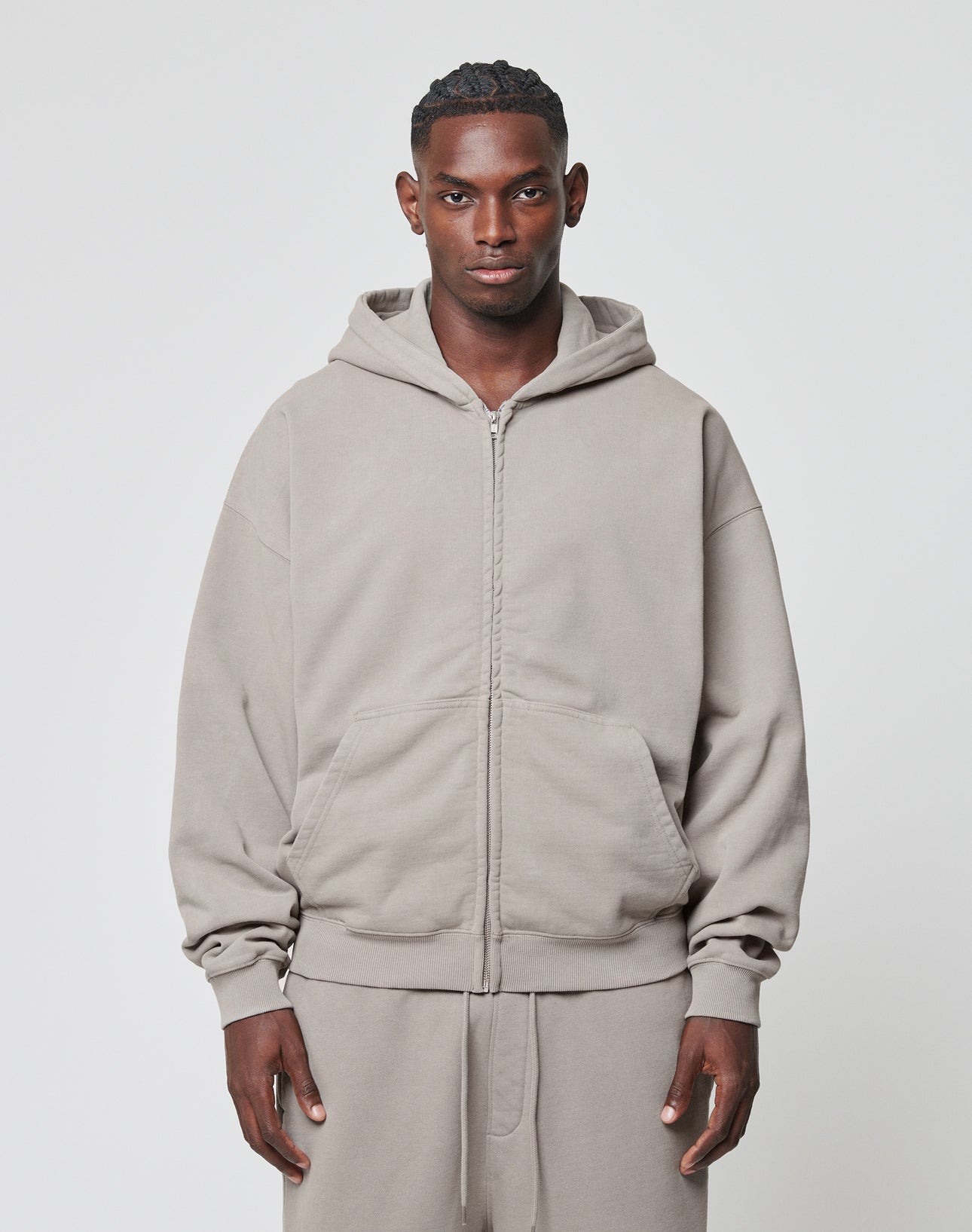 A man faces forward in a LIVE FAST DIE YOUNG Basic 510 Hooded Zip, light gray with front pockets and matching sweatpants, against a plain light background.