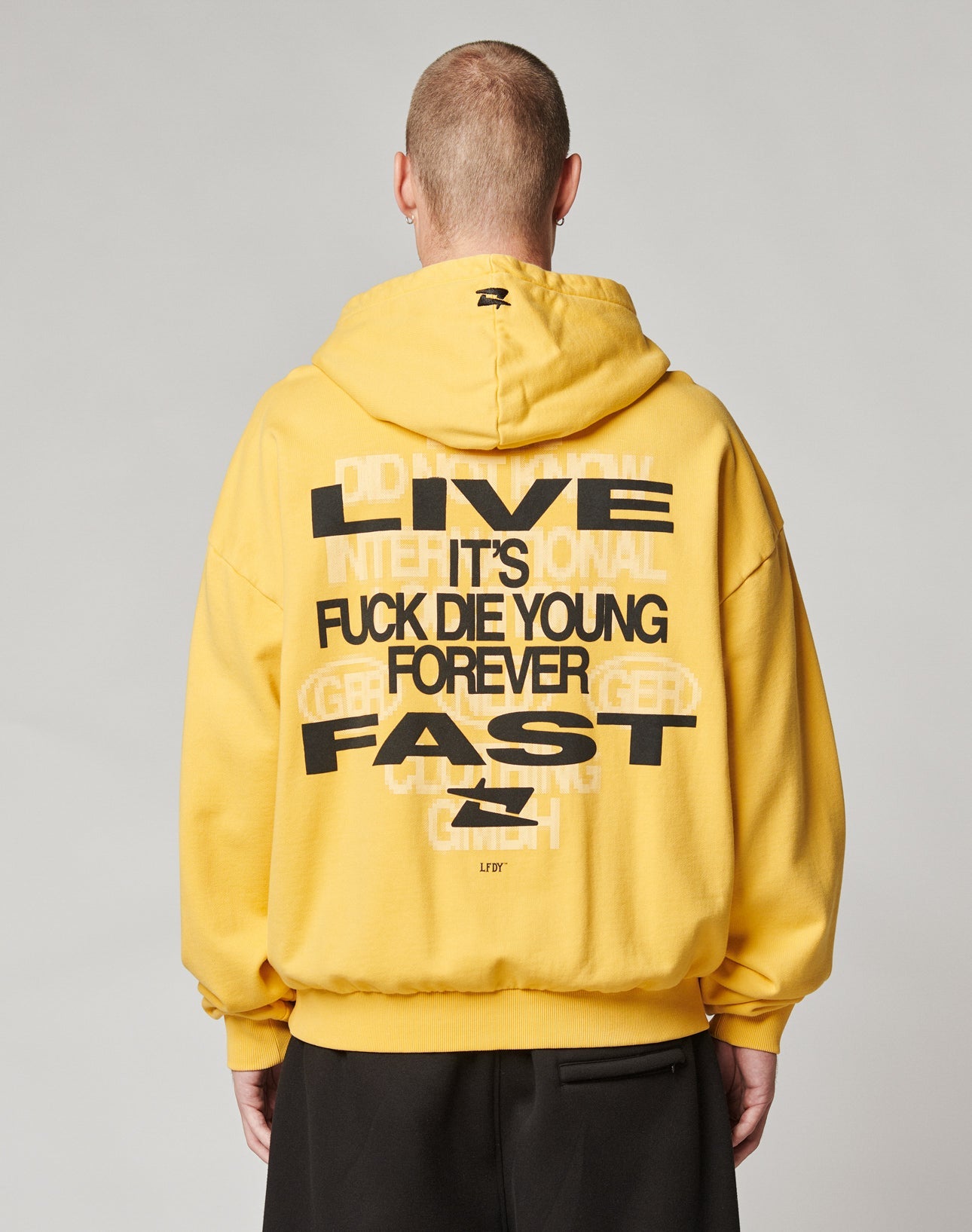 A person in an Oversize Fit yellow Print Over Hooded hoodie from LIVE FAST DIE YOUNG (100% cotton) with bold black and white front and back prints reading LIVE FAST, ITS FUCK DIE YOUNG FOREVER, shown from behind to highlight the back design.