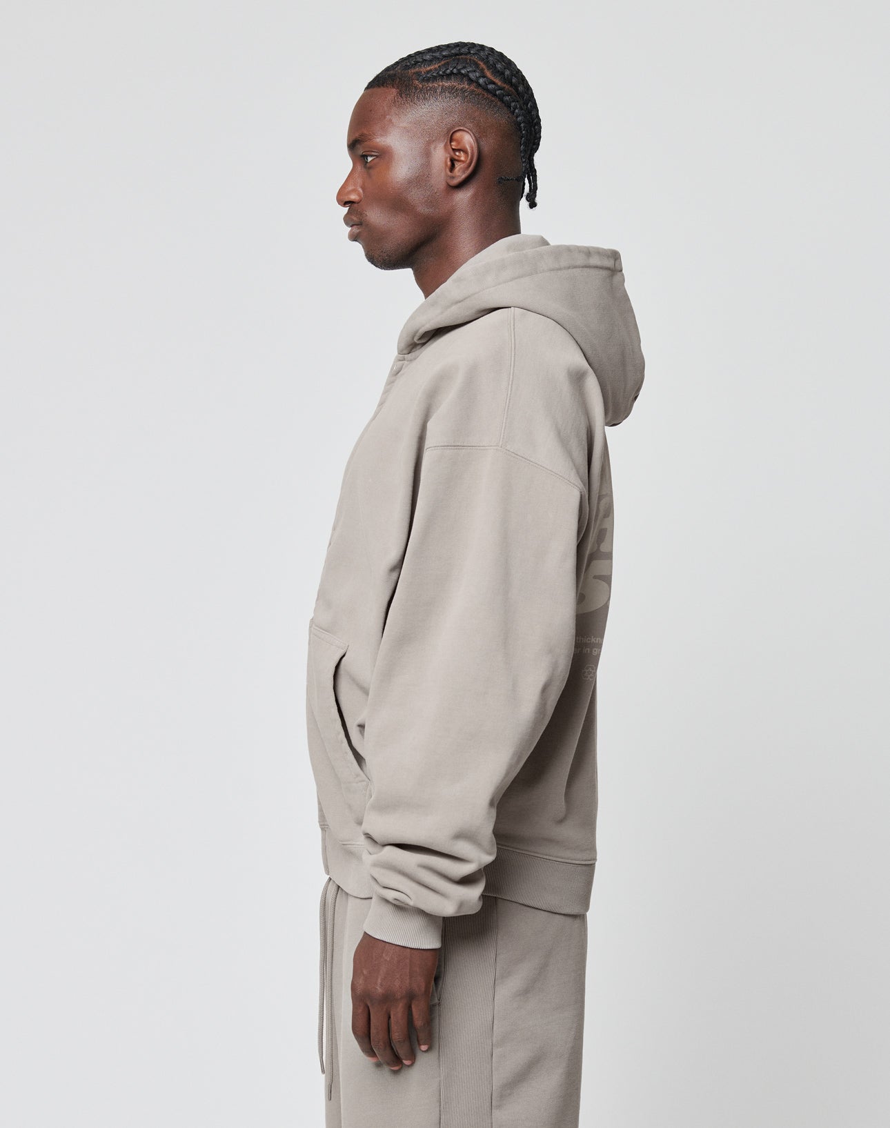 A person with braided hair stands in profile, facing left, wearing the taupe-colored Basic 510 Hooded Zip by LIVE FAST DIE YOUNG against a plain white background.
