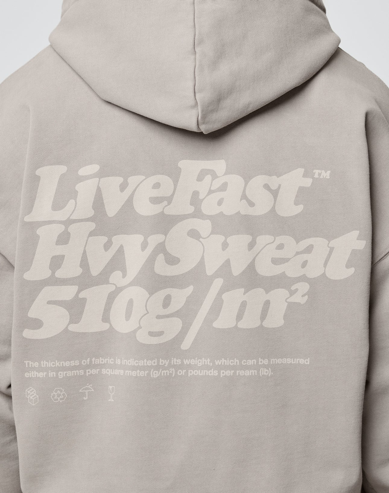 A person wears the LIVE FAST DIE YOUNG Basic 510 Hooded Zip in beige, featuring bold white “LiveFast HvySweat 510g/m²” text on the back, an oversize fit, and thick Baumwolle fabric highlighting its weight and quality.