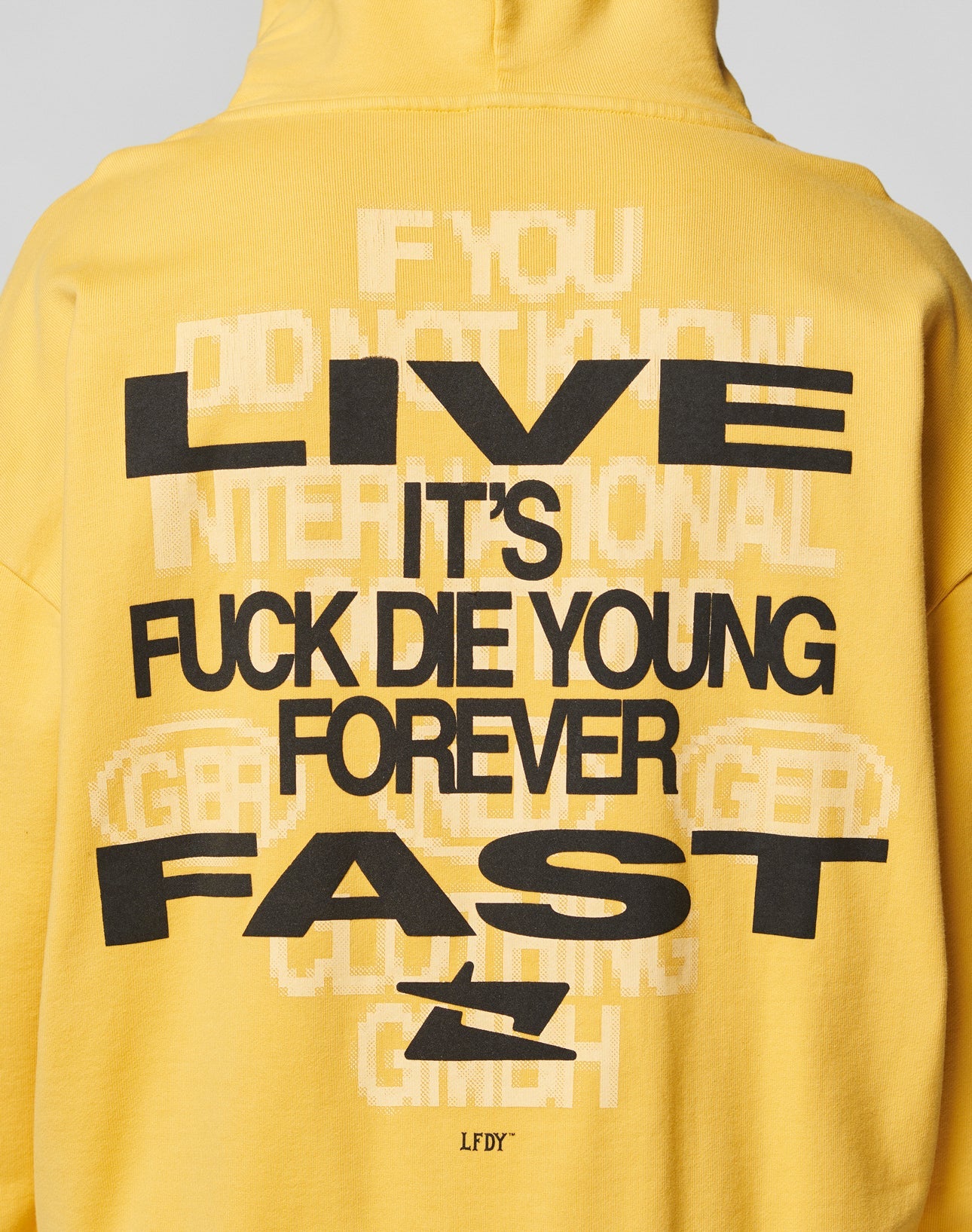 The Print Over Hooded by LIVE FAST DIE YOUNG is a yellow oversized hoodie made from 100% cotton, featuring bold black and white backprint text, faded details, and a small airplane icon near the hem.