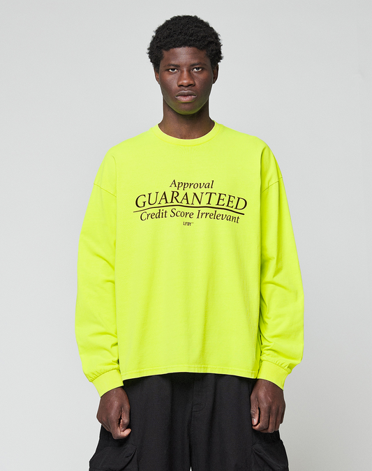 A person wears the LIVE FAST DIE YOUNG LFDY Real Est.8 Longsleeve in bright yellow, featuring bold "Approval GUARANTEED Credit Score Irrelevant" prints on front and back, against a plain light gray background. Made from 100% Baumwolle.