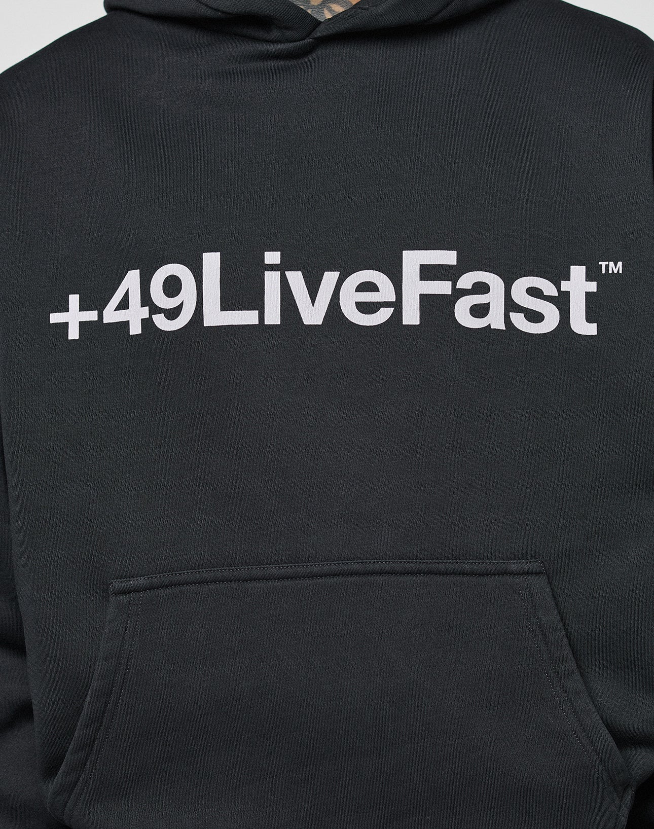 The Basic +49 Hooded by LIVE FAST DIE YOUNG is a black, oversized hoodie with a bold white +49LiveFast™ front print above the pocket, made from a soft cotton-polyester blend.
