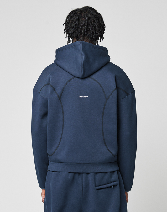 A person with short, twisted hair is seen from behind wearing the LFDY Active Fleece Hooded Zip by LIVE FAST DIE YOUNG—a navy blue oversize sweatshirt with black curved seams and a small white logo print at the center back, made of Baumwolle.