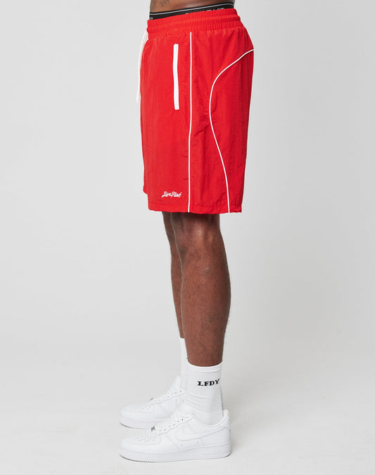 A person in bright red Beach Shorts by LIVE FAST DIE YOUNG, featuring an elastic waistband and white trim, along with LFDY white socks and white sneakers, stands in side profile against a plain white background.