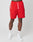 A person models LIVE FAST DIE YOUNG Beach Shorts—bright red with an elastic waistband and white drawstrings—paired with white crew socks and sneakers, against a light gray backdrop. Only the lower half of the body is visible.
