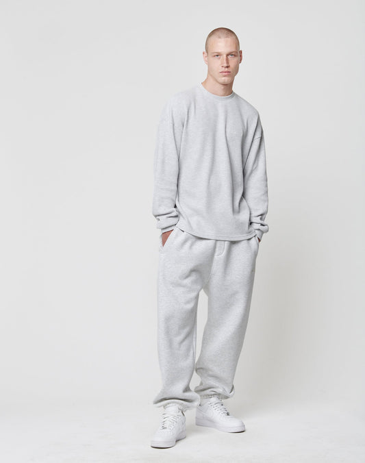 A person stands against a white background wearing the LIVE FAST DIE YOUNG Basic Script Waffle Longsleeve in light gray, with matching sweatpants and white sneakers, hands in pockets and a neutral expression.